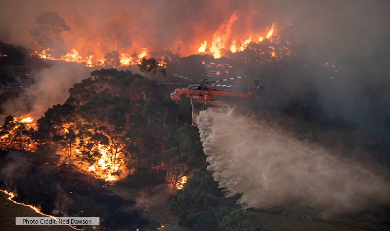 helicopter dispensing water on wildfire below